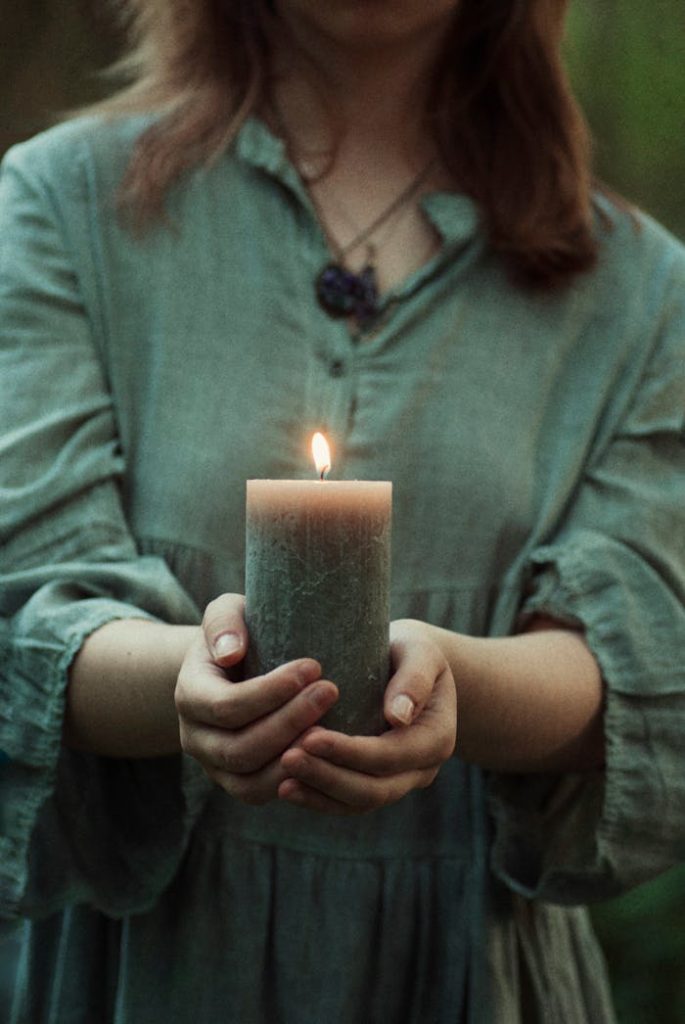 pexels photo 12943877 A woman gently holding a lit candle, evoking peace and tranquility. Perfect for calming visuals.