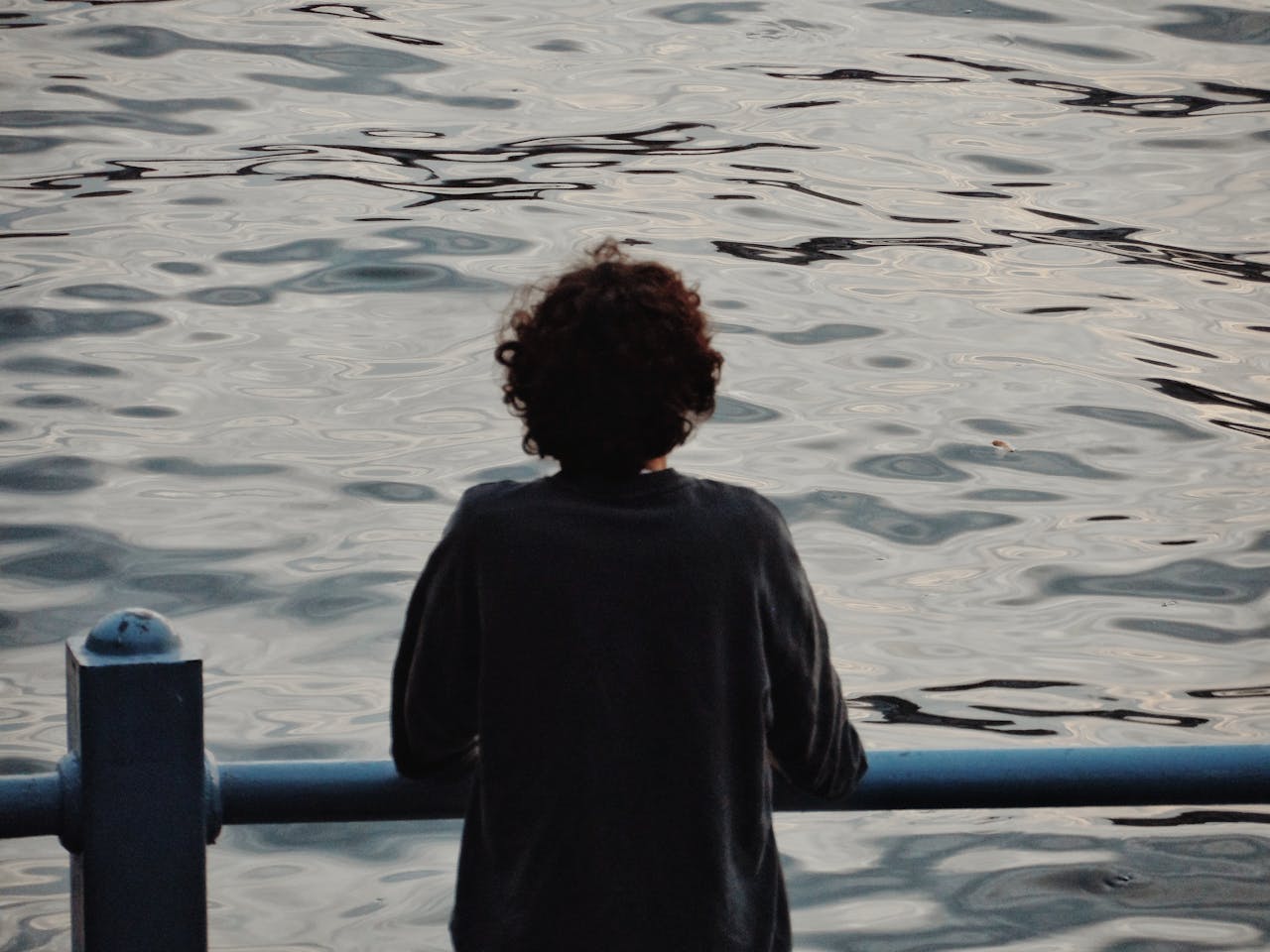 A solitary person gazes thoughtfully over calm rippling water, creating a serene and reflective mood.